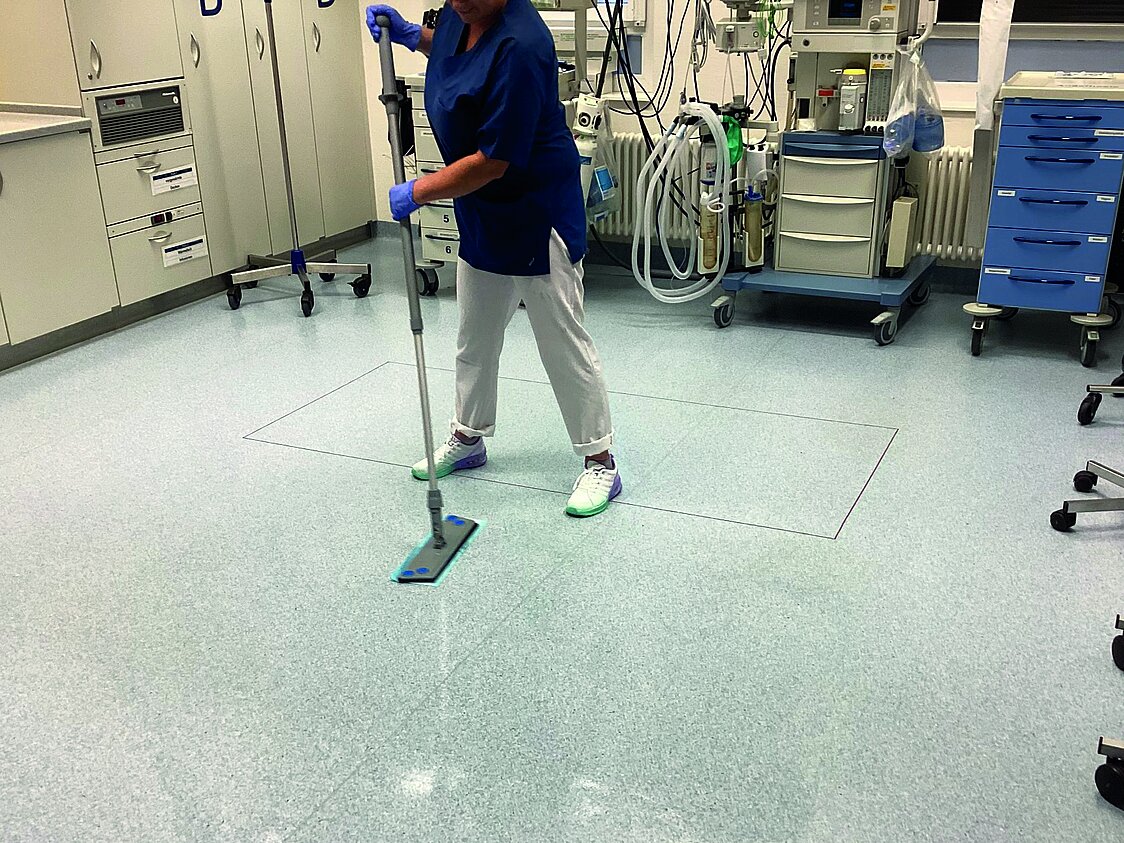 Eine Person in Arbeitskleidung wischt mit dem Mikrozid Power Mop von Schülke den Boden einer medizinischen Einrichtung.